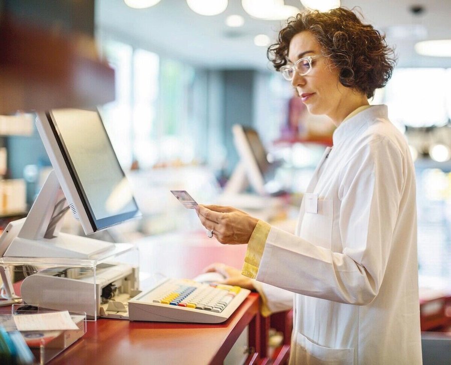 Female_pharmacist_adding_customers_medical_membership_card_details_in_the_computer_database._Mature_woman_chemist_workin