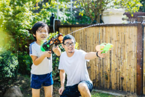 Vater und Sohn spielen mit Wasserpistolen im Garten