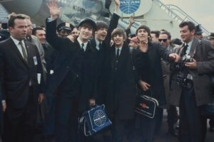 The_Beatles_arrive_at_New_York's_John_F._Kennedy_International_Airport_(formerly_Idlewild),_in_New_York,_Feb._7,_1964._From_left:_John_Lennon_(waving),_Paul_McCartney,_Ringo_Starr_and_George_Harrison._(AP_Photo)