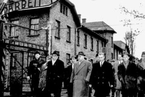 The_group_of_the_Frankfurt_jury_court_and_several_journalists_are_passing_the_camp_gate_with_the_words_‘Arbeit_macht_frei’_(work_brings_freedom)._The_first_local_inspection_during_the_Auschwitz_Trial_took_place_on_the_grounds_of_the_former_concentration_c