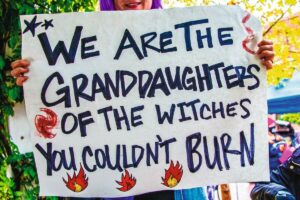 2021-10-02_Tulsa_USA_-_Woman_with_purple_hair_holding_sign_reading_We_are_the_Granddaughters_of_the_Witches_You_couldn't_burn_on_bright_fall_day_a_rep